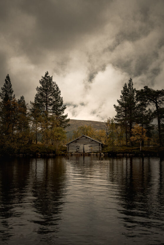 An old wooden hut by a mountain lake with autumn colours
